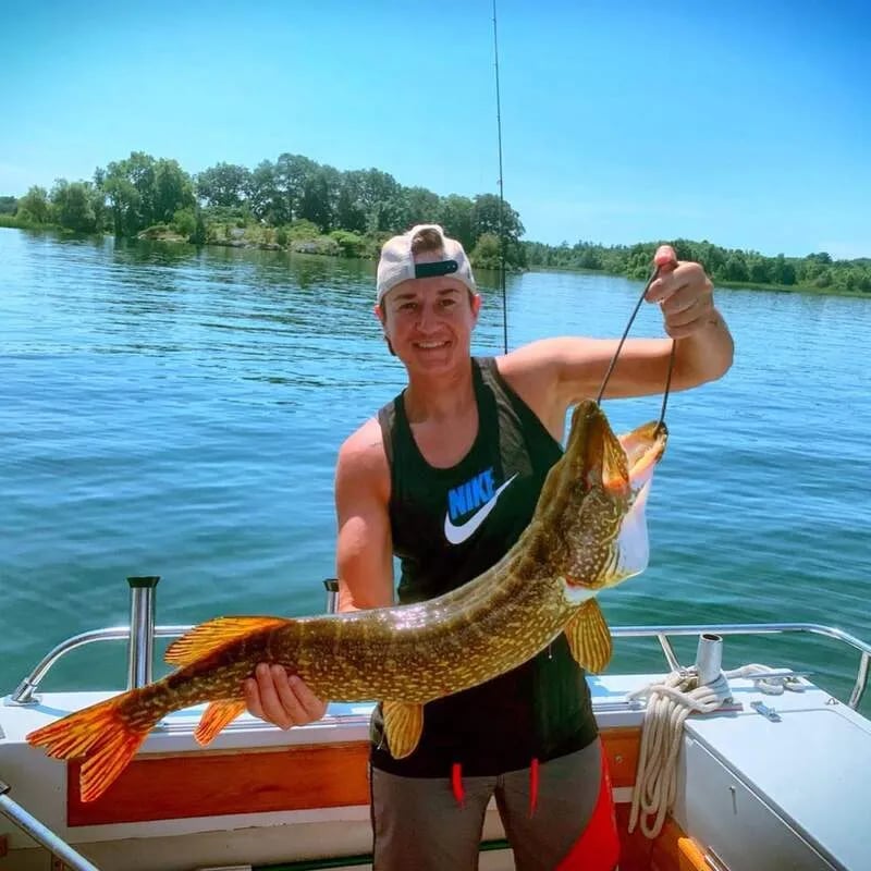 Woman angler holding a large Northern Pike on a boat.