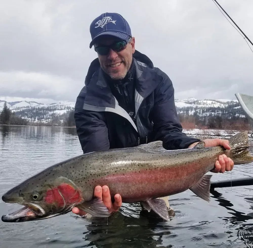 Two bearded anglers holding a large Steelhead in a river.