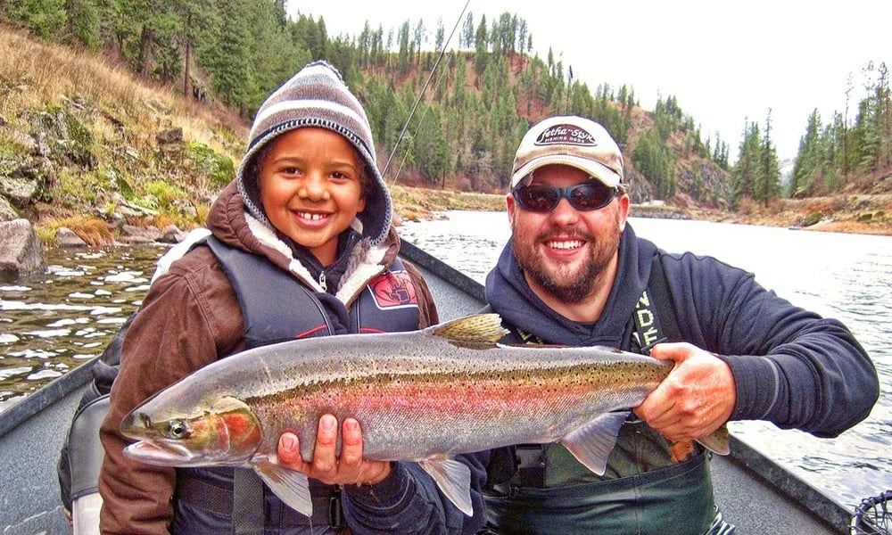 Man and child smiling, holding a Steelhead in a drift boat.