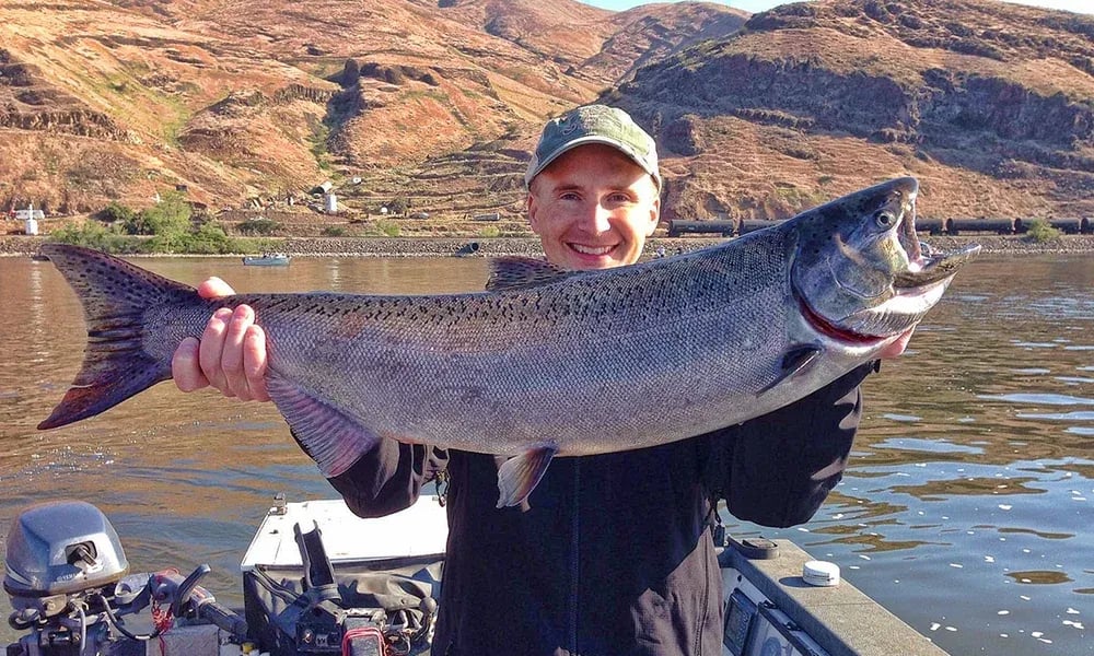 Angler in sunglasses holding a large Steelhead in a drift boat.