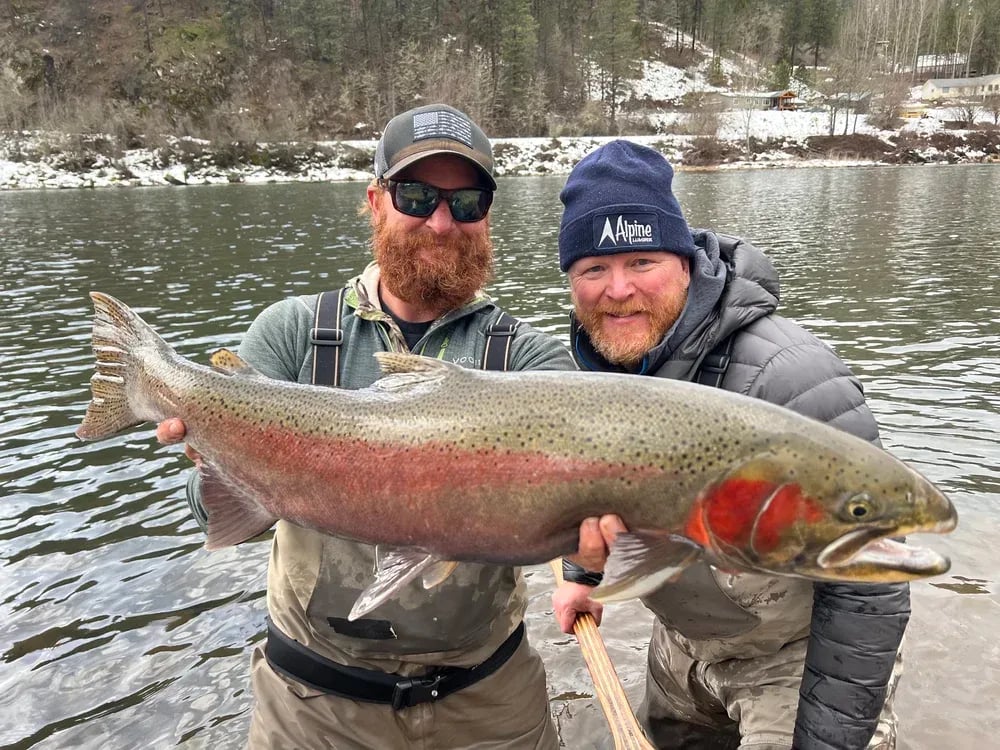 Two anglers in a boat smiling, holding a large Steelhead.