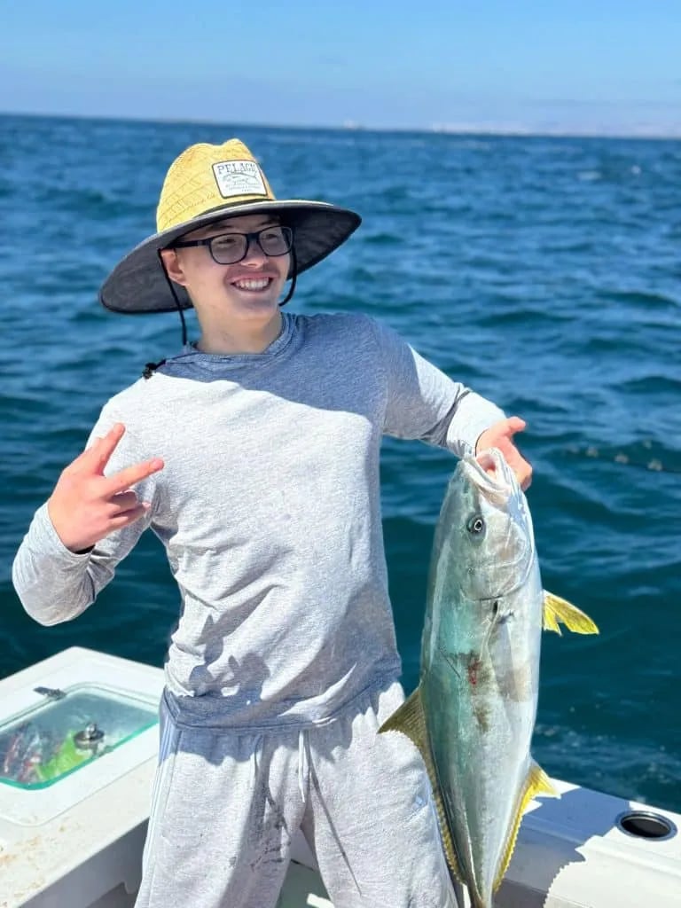 Angler holding a Yellowtail on a boat under a clear sky.