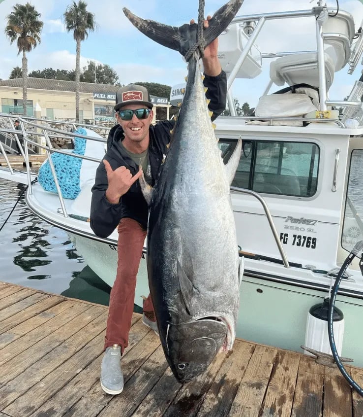 Three anglers on a boat holding a mixed catch of Yellowtail and Tuna at the dock.
