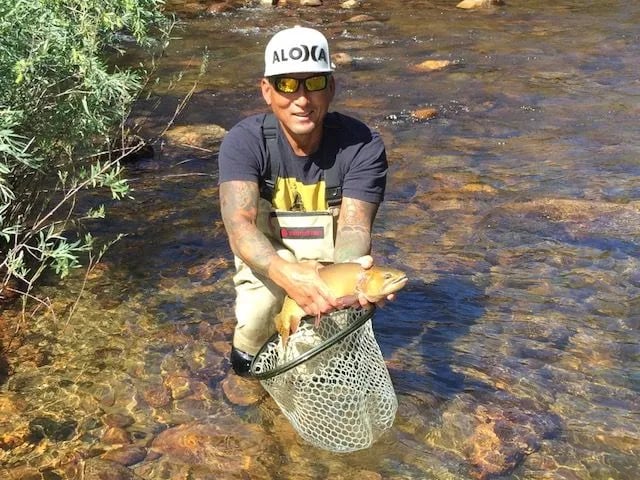 Angler in waders holding a Brown Trout in a net in a shallow river