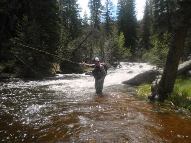 Angler wading in a rocky river, casting a fly rod upstream