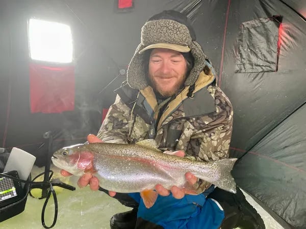 Angler holding a large Rainbow Trout inside an ice fishing tent