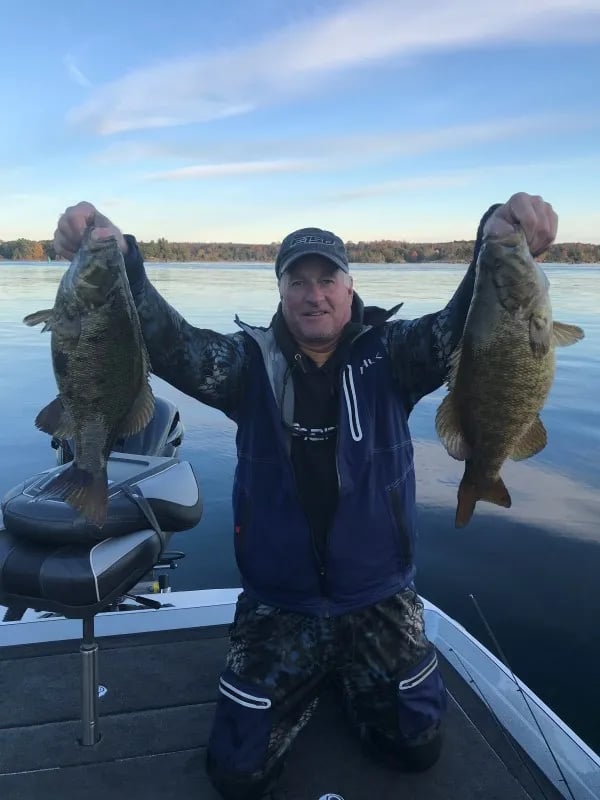 Three anglers on a boat holding multiple Walleye under a clear blue sky.