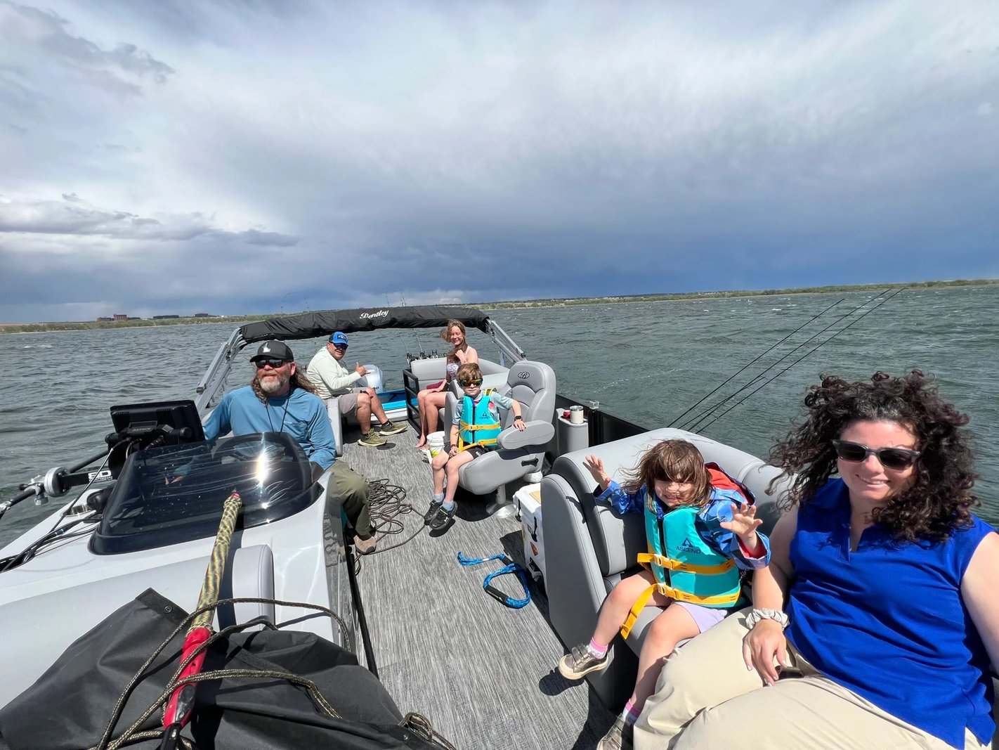 Group of people relaxing on a pontoon boat under a cloudy sky.