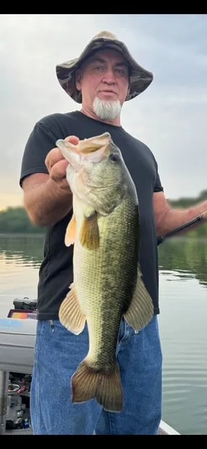 Man in sunglasses and life vest holding a large Largemouth Bass on a boat