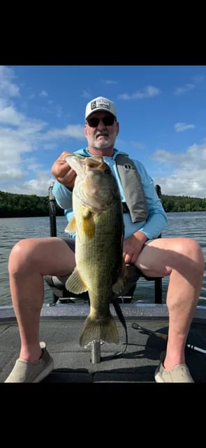 Man in a black jacket and cap holding a large Largemouth Bass on the water