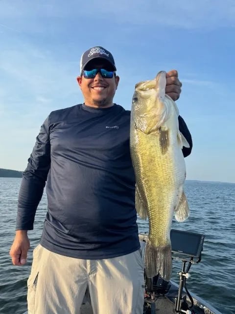 Woman smiling, holding a large Largemouth Bass on a boat