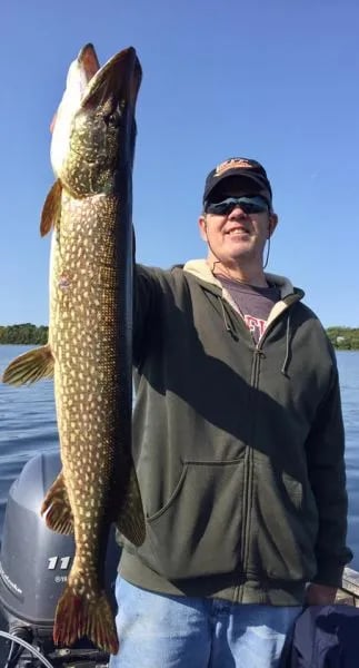 Woman in sunglasses holding a large Lake Trout against a bright blue sky.
