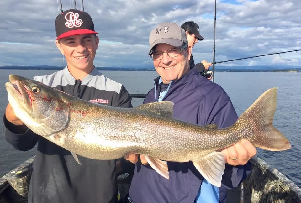 Family of three holding a large Lake Trout on a boat.