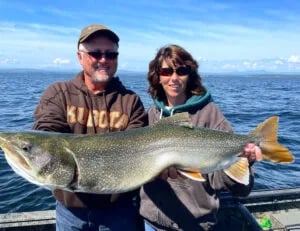 Man in sunglasses and a cap holding a very large Northern Pike over the water.