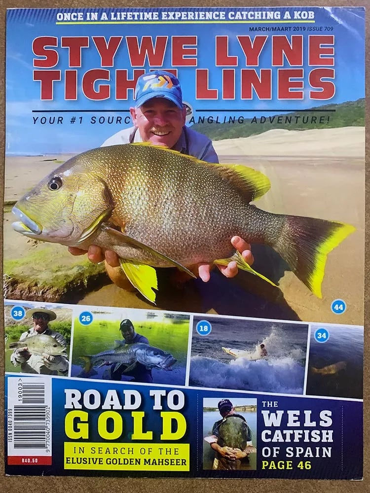 Two anglers on a sunny beach, one fighting a fish with a bent rod.