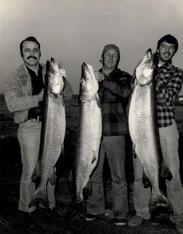 Smiling angler in a red hat holding a large Musky on a boat