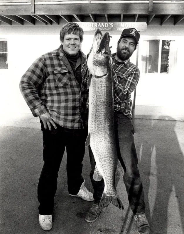 Two men in plaid shirts holding a massive Musky in a black and white photo