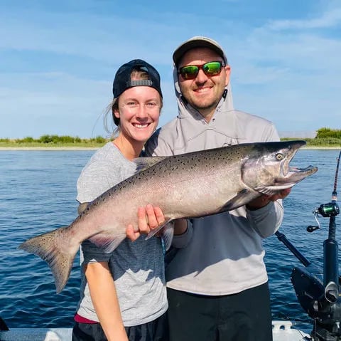 Angler on a boat holding a very large, dark King Salmon with an open mouth.