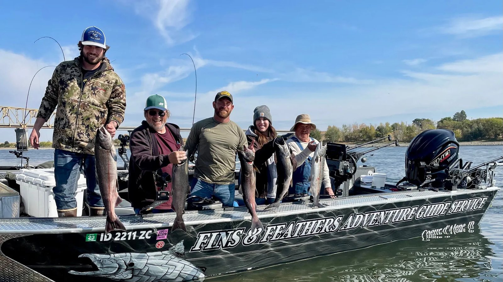 Group of anglers on a boat holding multiple King Salmon, with "FINS N FEATHERS" visible on the boat side.