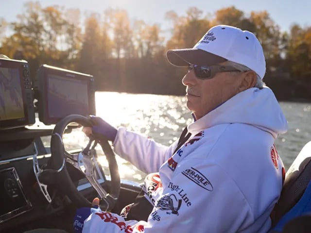 Angler in a red shirt and sunglasses holding a Largemouth Bass from a boat.
