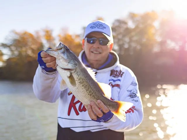 Angler in an orange shirt holding two Crappie over a lake.