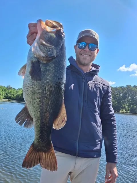 Adult and child smiling, holding a large Largemouth Bass on a sunny lake.