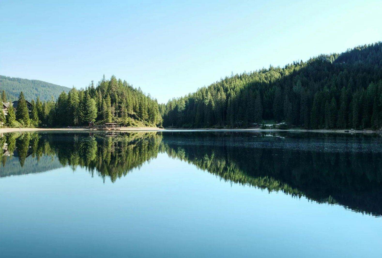 Calm lake reflecting forested hills under a clear sky.