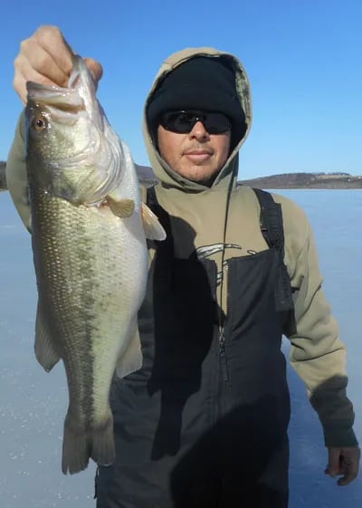 Angler in a winter coat holding a largemouth bass on a frozen lake.
