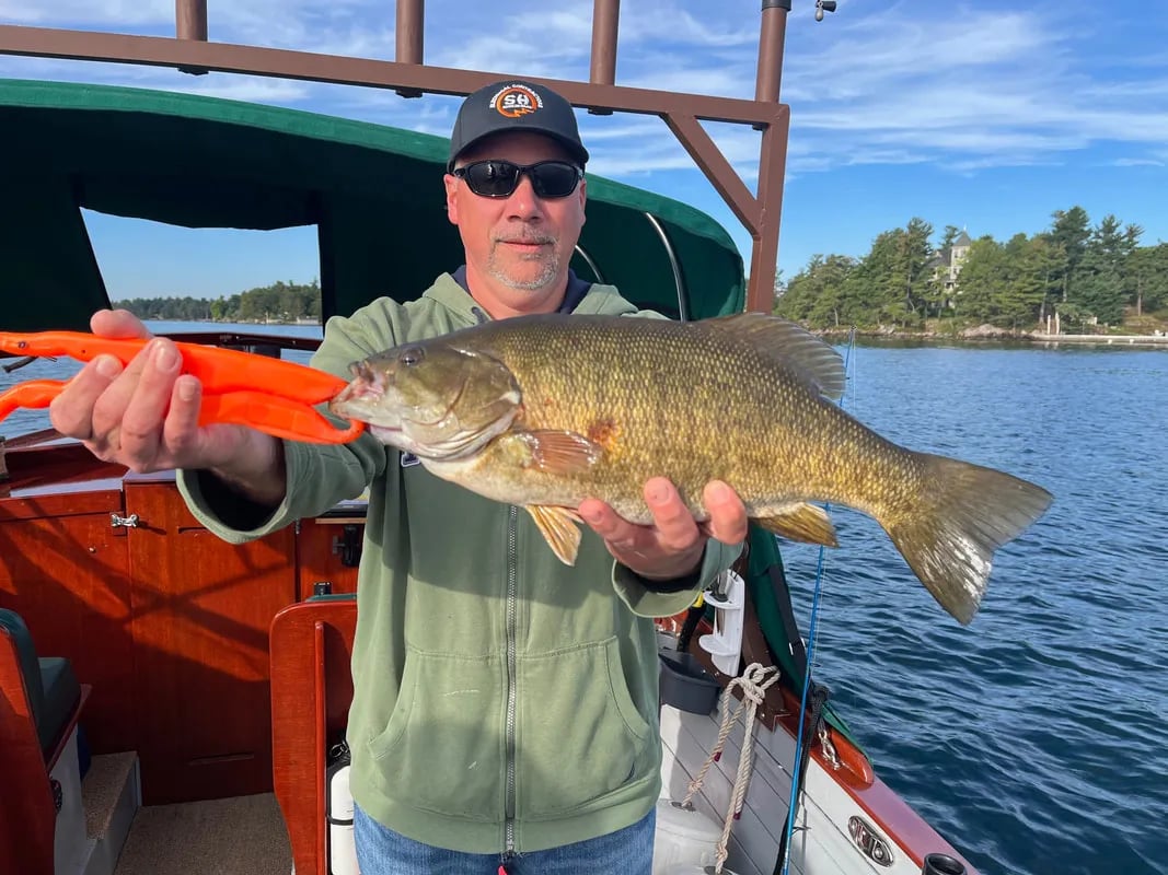 Angler on a boat holding a large smallmouth bass with a fish gripper