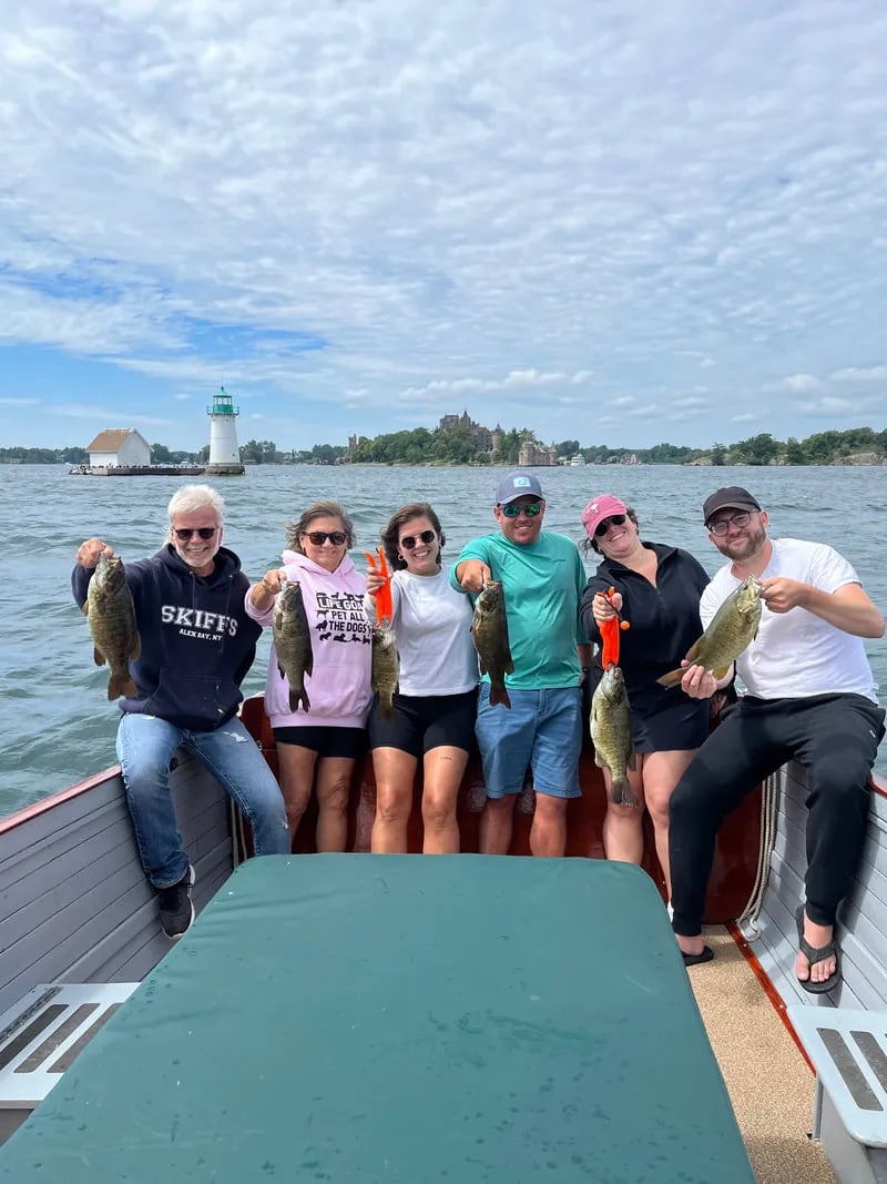 Group of six anglers on a boat holding their smallmouth bass catches with a historic castle in the background