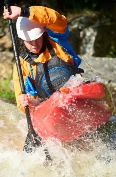 Kayaker in an orange jacket paddling through whitewater.