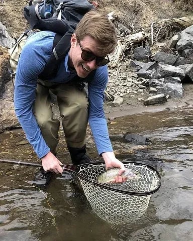 Smiling angler holding a Rainbow Trout in a net in a river.