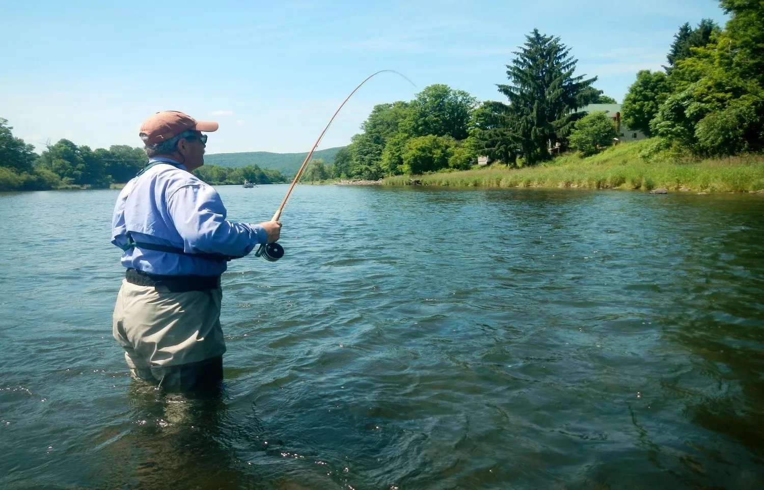 Angler wading and casting a fly rod in a wide river.
