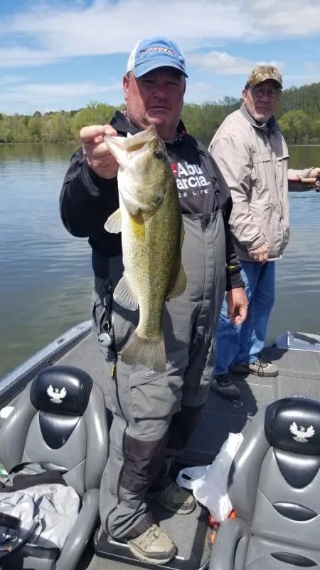 Young boy smiling, holding a largemouth bass on a boat.