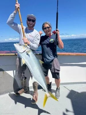 Two anglers on a boat deck holding a large Yellowtail