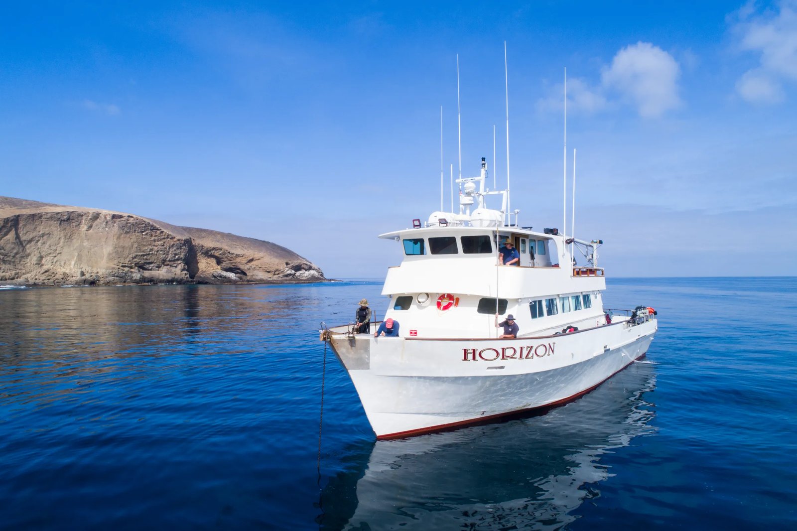 The 'Horizon' charter boat underway on calm blue water with a rocky island in the background