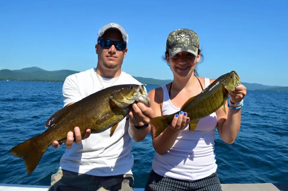Two children on a boat proudly holding a largemouth bass