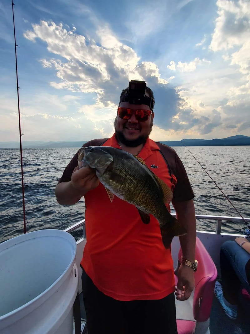 Angler in sunglasses holding a large Lake Trout on a boat with mountains in the background