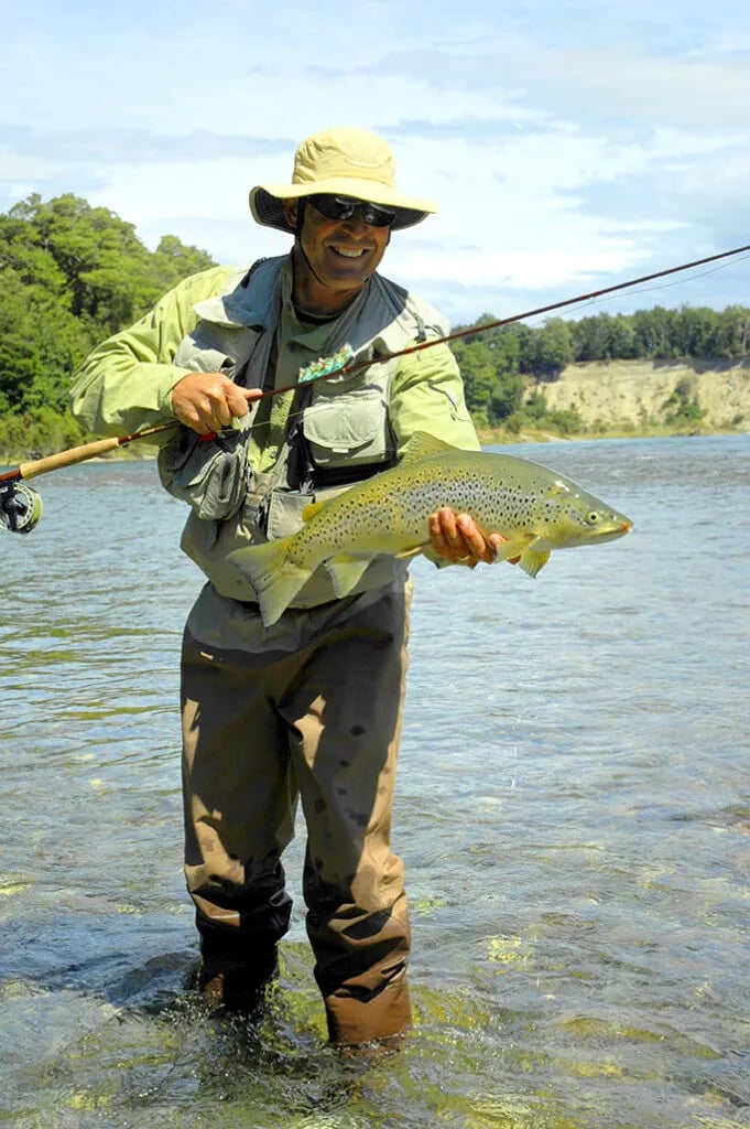 Angler wading in clear, rocky river water with a fly rod.