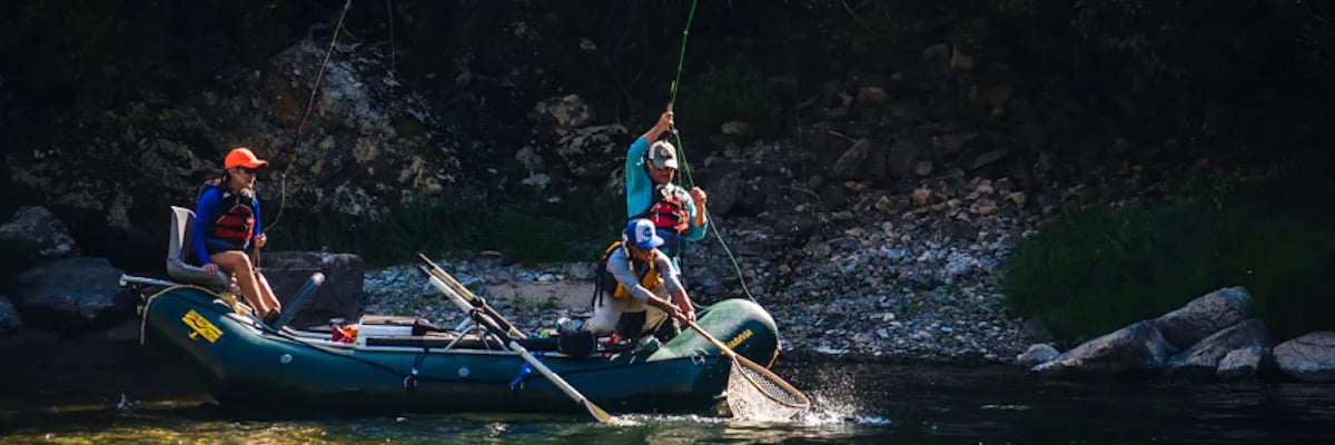 Angler casting a fly rod from a green inflatable raft on a river.