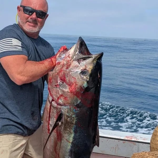 Angler holding a large, bloody Bluefin Tuna on a boat.