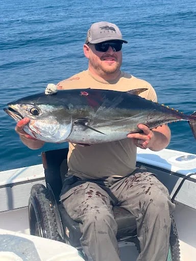Angler in a wheelchair holding a Yellowfin Tuna on a boat.