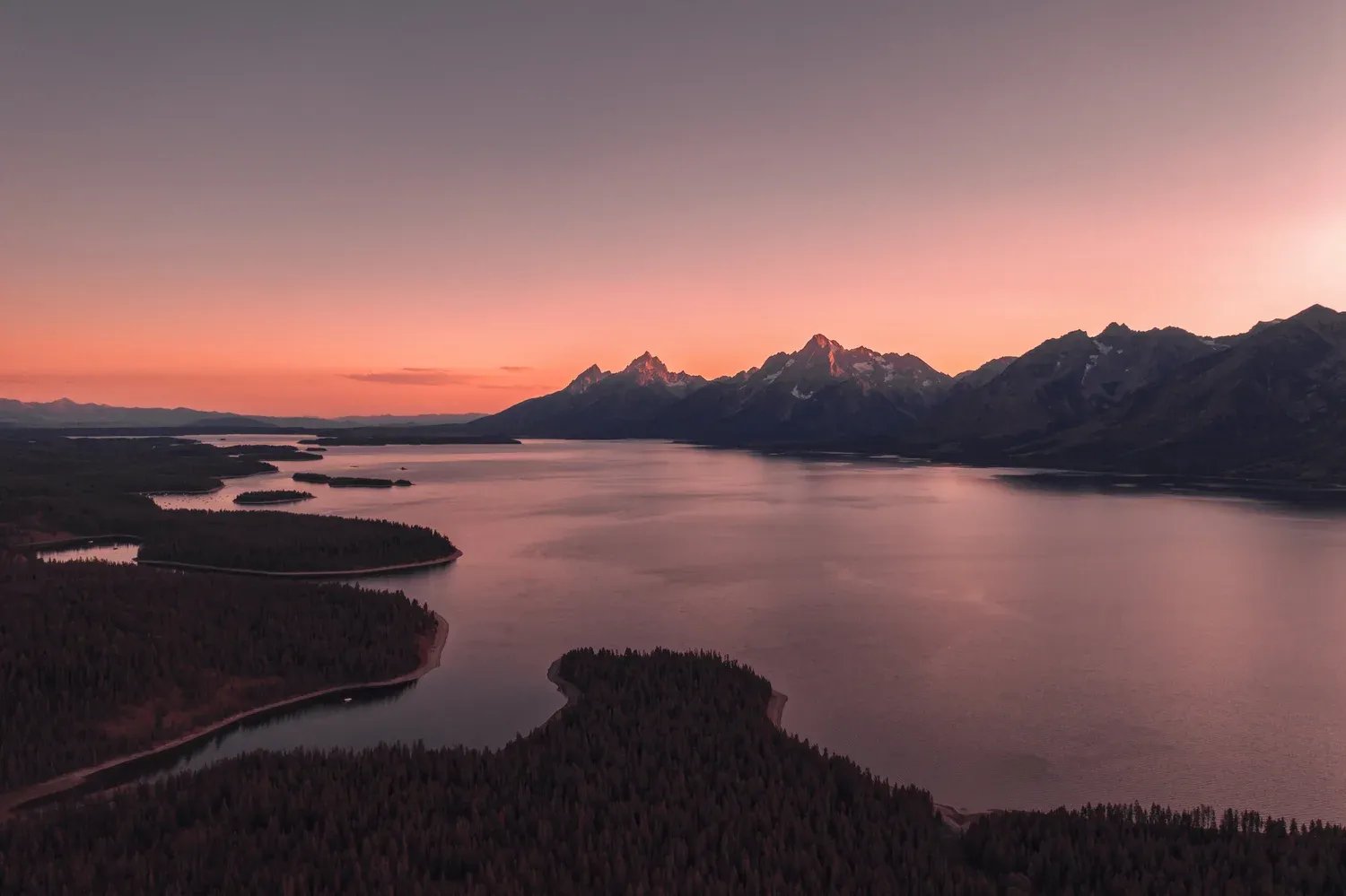 Sunset over a large lake with mountains and forested shorelines.