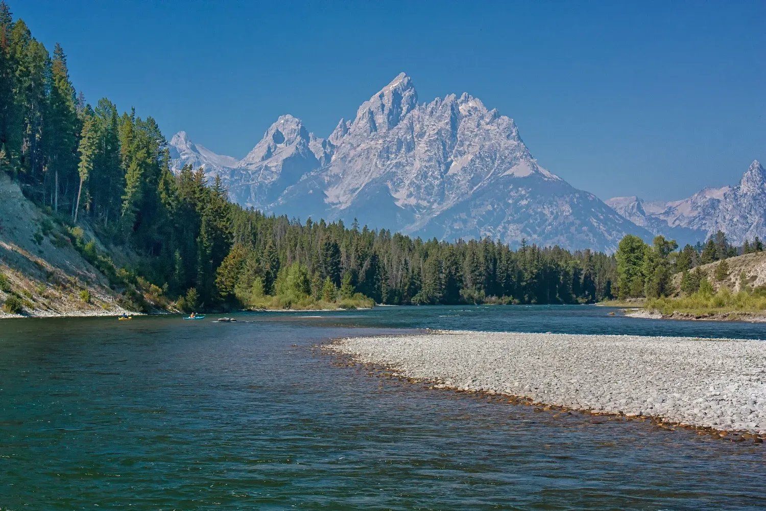 River flowing through a forest with a prominent mountain peak in the background.