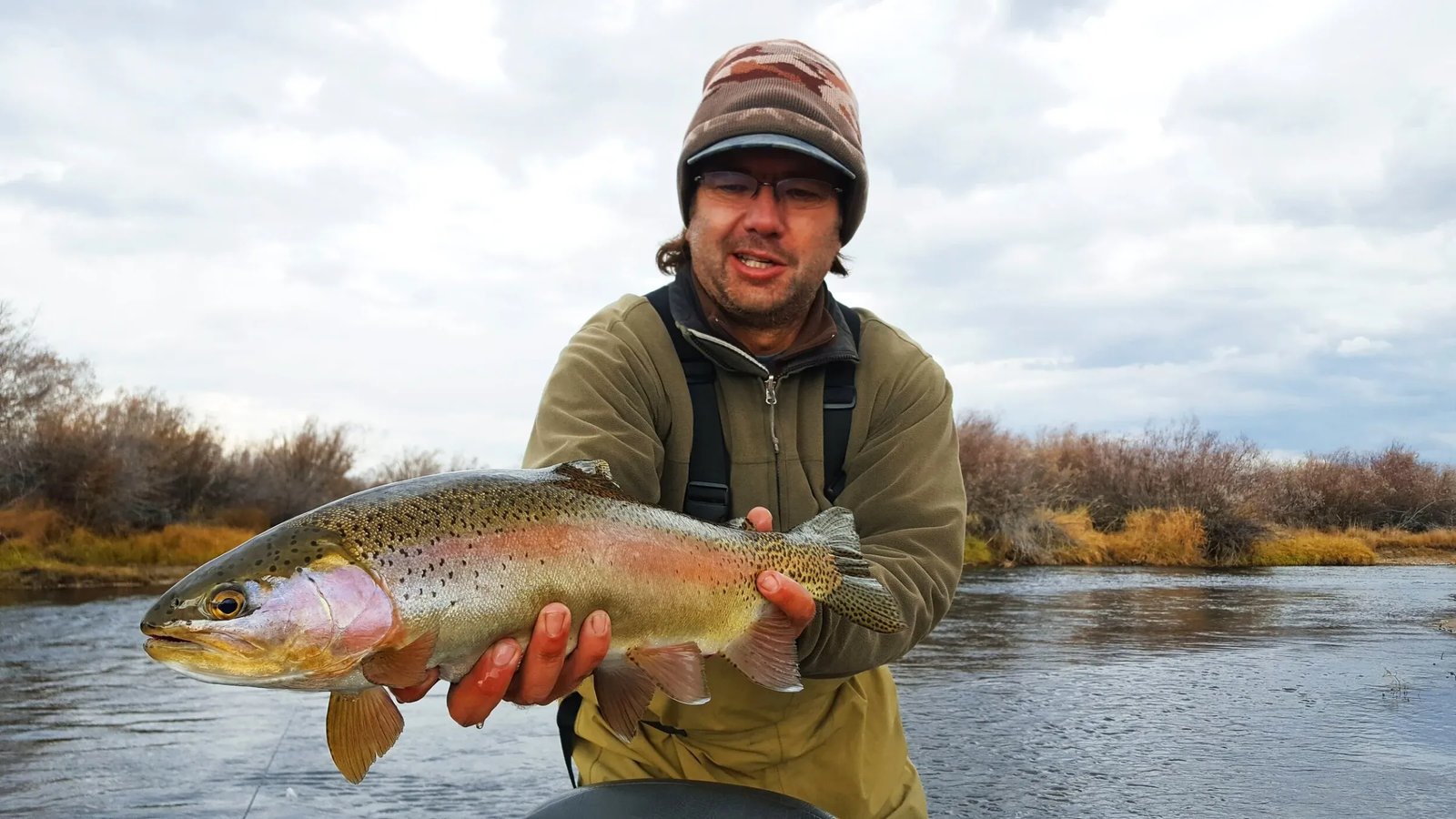 Angler holding a large Rainbow Trout in a river.