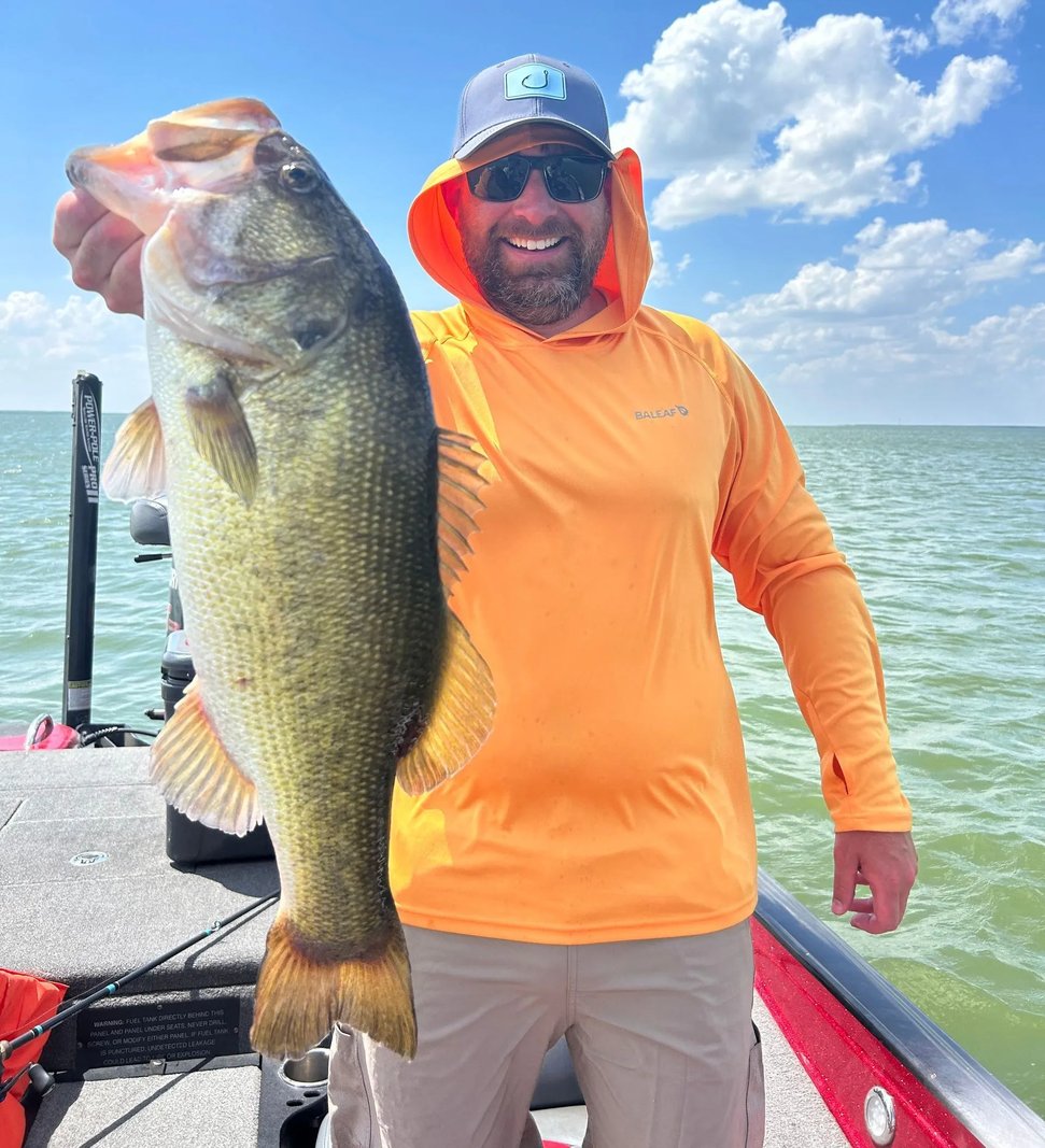 Bass boat with a single angler running across a lake with forested hills in the background