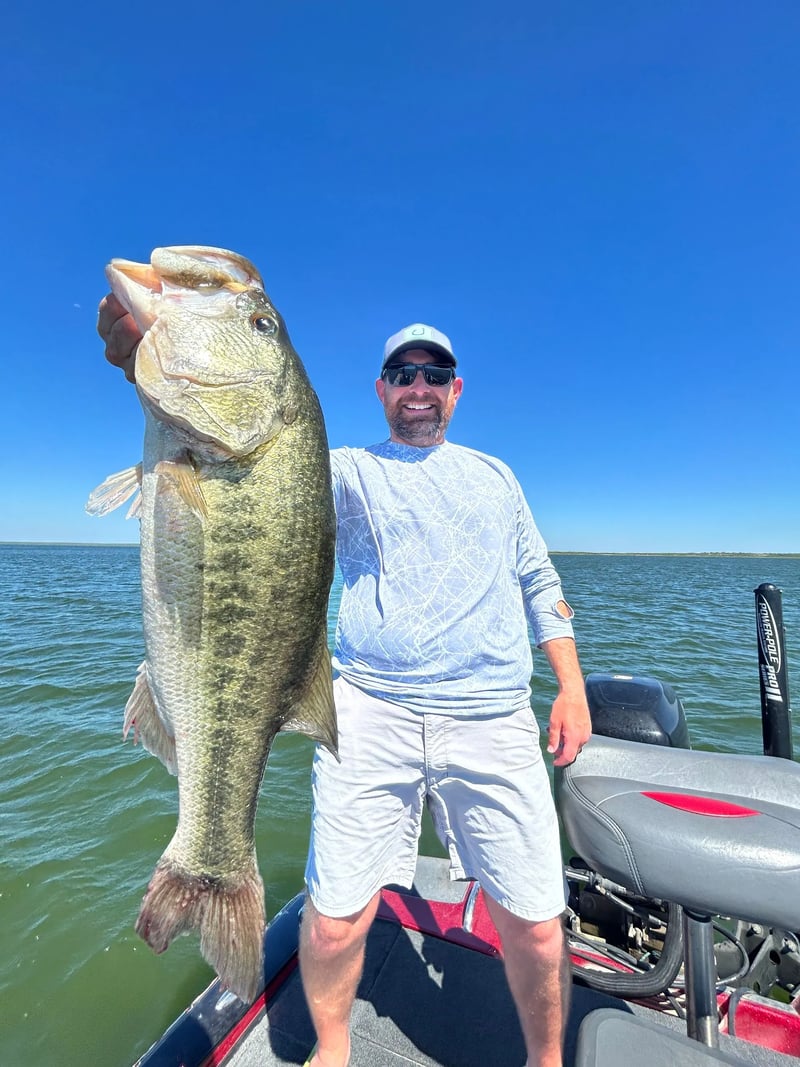 Angler in orange shirt holding a large Largemouth Bass on a boat under a sunny sky