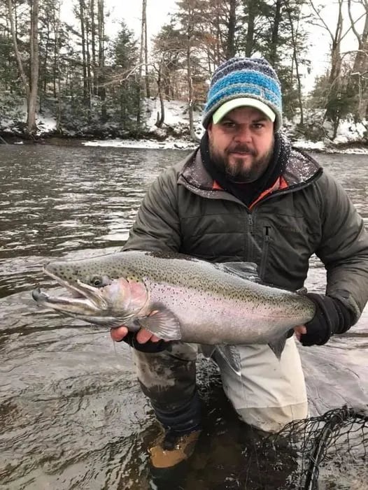 Angler in waders holding a large Steelhead in a snowy river.