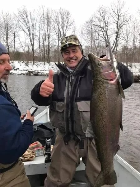 Angler on a boat giving a thumbs up while holding a large Steelhead.