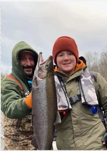 Two anglers on a boat holding a large Steelhead.